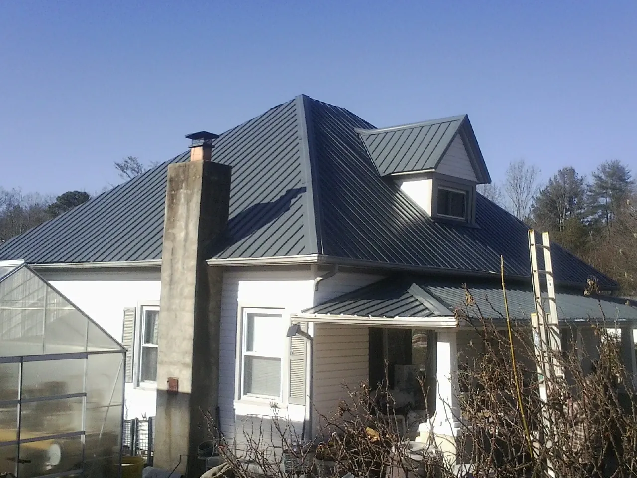 Dark blue standing seam metal roof on a white farmhouse with dormer — Slate & Tile Roof Repair by Roofing Brothers in Cascade