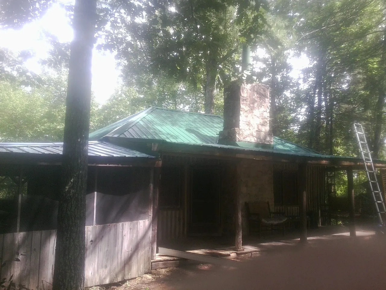 Green metal roof and stone chimney above a log cabin porch in Cascade